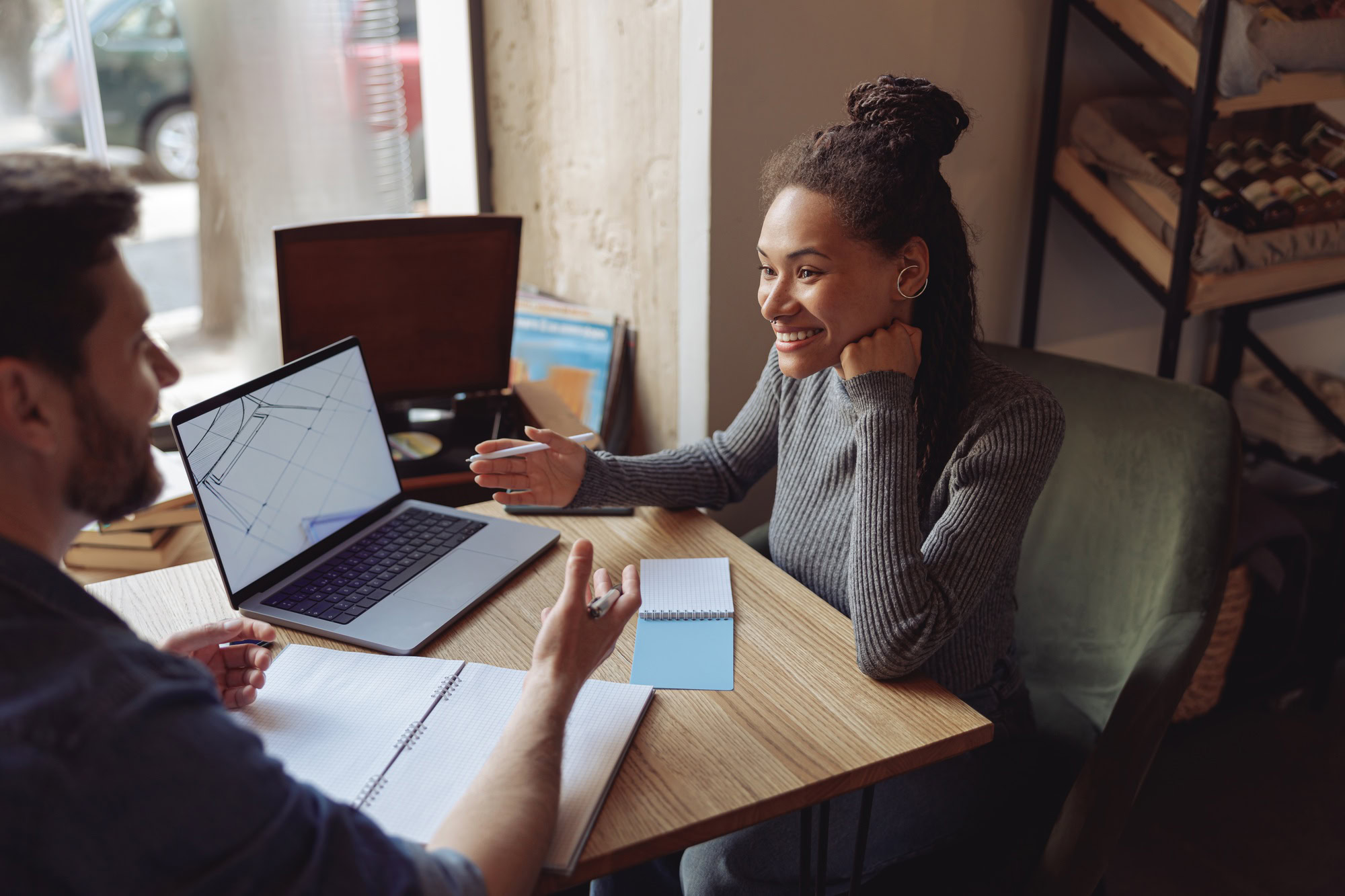 Cheerful young stylish woman at meeting with male partner in cafe. Discussing startup at laptop.